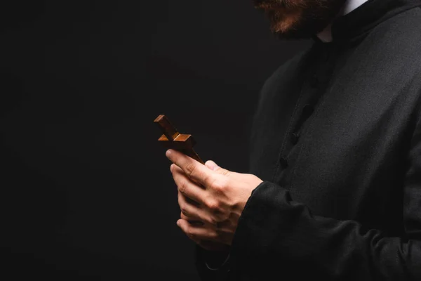 Cropped view of priest holding cross isolated on black — Stock Photo