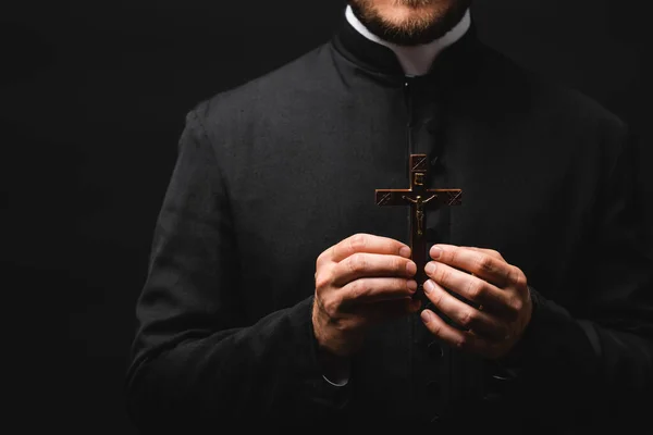 Cropped view of pastor holding wooden cross isolated on black — Stock Photo