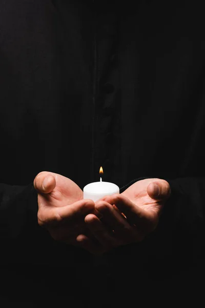 Vista cortada de pastor segurando vela ardente isolado em preto — Fotografia de Stock