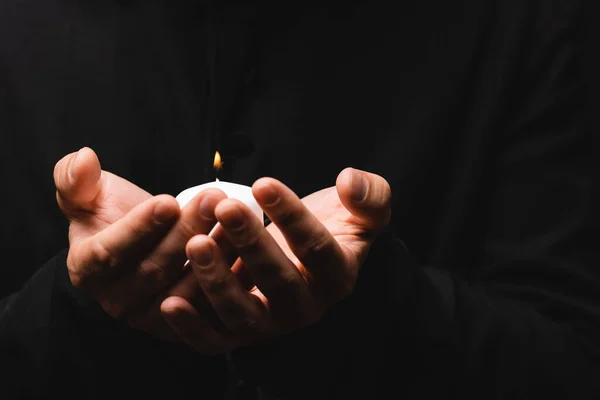 Partial view of priest holding burning candle isolated on black — Stock Photo