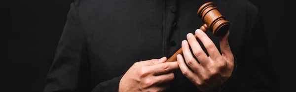 Panoramic crop of priest holding wooden gavel isolated on black — Stock Photo