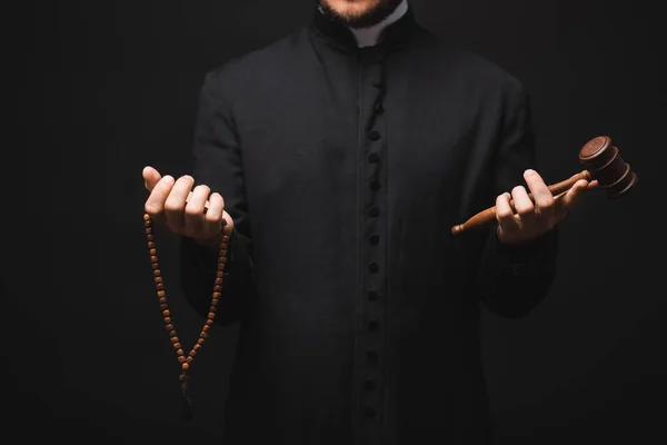 Vista recortada del sacerdote sosteniendo martillo de madera y cuentas de rosario en manos aisladas en negro - foto de stock