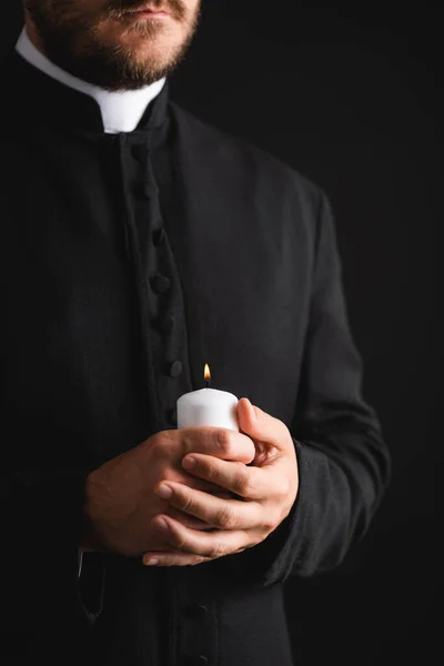 Обрезанный вид бородатого священника, держащего горящую свечу в руках, изолированных на черном — стоковое фото