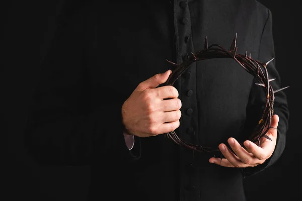 Cropped view of priest holding sharp wreath with spikes isolated on black — Stock Photo