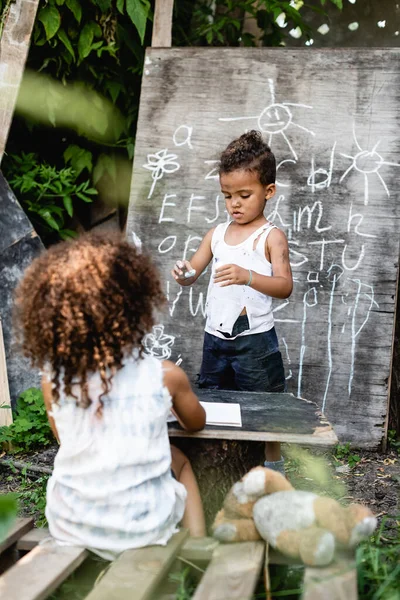 Foyer sélectif de pauvre gamin afro-américain debout près de tableau noir et bouclé garçon — Photo de stock