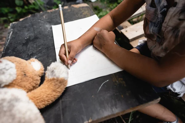 Vista parcial del niño afroamericano sosteniendo lápiz mientras escribe en papel - foto de stock