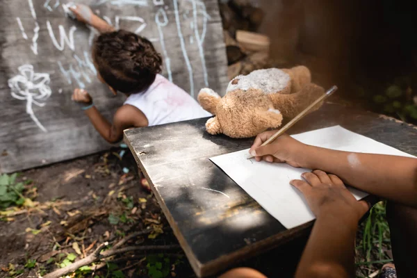 Visão parcial da criança afro-americana escrevendo perto de criança e quadro — Fotografia de Stock