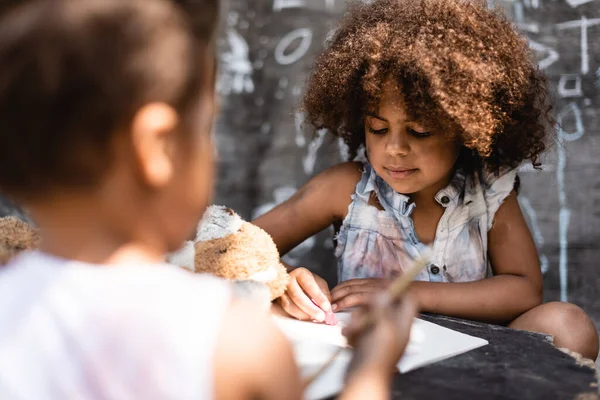 Selective focus of curly and poor african american child writing near brother — Stock Photo