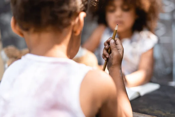 Selektiver Fokus armer afrikanisch-amerikanischer Kinder, die Bleistift in der Nähe ihrer Schwester halten — Stockfoto