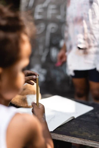 Enfoque selectivo de pobre afroamericano chico sosteniendo lápiz cerca de hermana - foto de stock