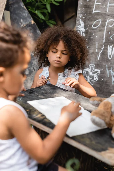 Foco seletivo de criança afro-americana pobre olhando para papel em branco perto do irmão — Fotografia de Stock