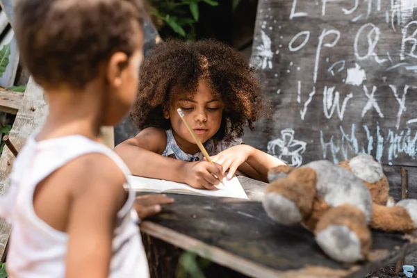 Enfoque selectivo de los niños afroamericanos pobres escribiendo en papel cerca de hermano - foto de stock