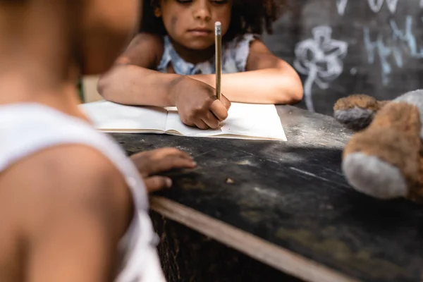 Abgeschnittene Ansicht eines armen afrikanisch-amerikanischen Kindes, das in der Nähe seines Bruders auf Papier schreibt — Stockfoto