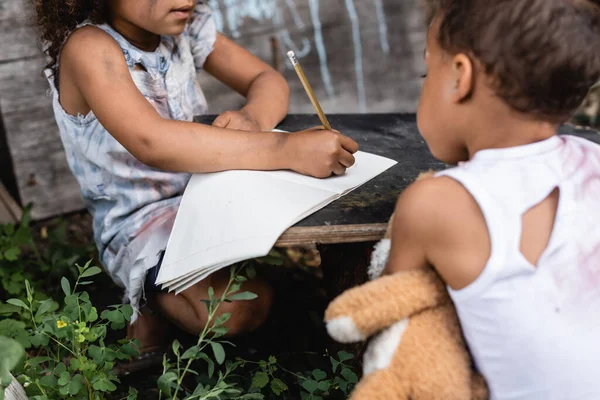 Частичный взгляд на бедного африканского ребенка, который пишет в блокноте рядом с братом — стоковое фото