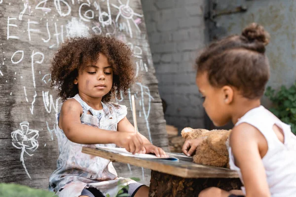 Selective focus of poor african american kid writing in notebook near brother outside — Stock Photo