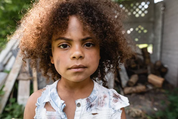 Selective focus of poor african american child in torn clothes looking at camera outside — Stock Photo