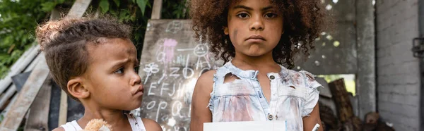 Panoramic crop of sad and poor african american kid near upset brother outside — Stock Photo