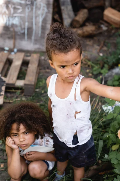 Selective focus of poor african american boy in torn clothes standing near sad sister — Stock Photo