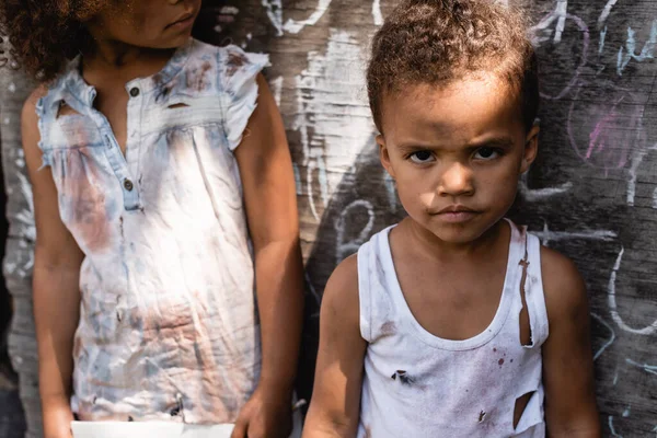 Poor african american kid in torn clothes standing with brother near chalkboard — Stock Photo