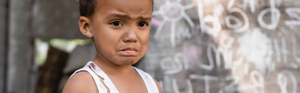 Concepto panorámico de niño afroamericano pobre llorando cerca de pizarra - foto de stock