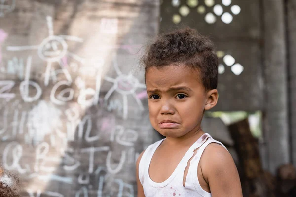 Foco seletivo de menino afro-americano pobre chorando perto de quadro-negro — Fotografia de Stock