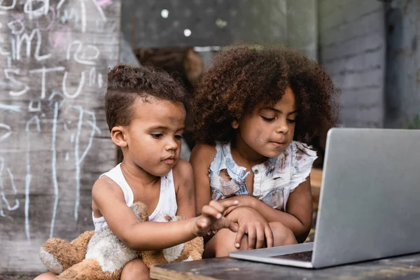 Selektiver Fokus armer afrikanisch-amerikanischer Kinder, die Laptop draußen benutzen — Stockfoto