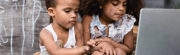 Панорамный урожай бедных африканских американских детей, смотрящих на ноутбук снаружи — стоковое фото