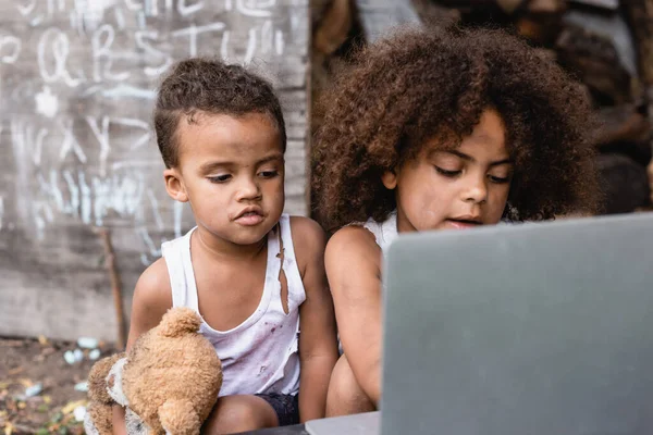 Избирательный фокус бедных африканских американских детей, смотрящих на ноутбук снаружи — стоковое фото