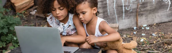 Panoramic orientation of poor african american kids using laptop outside — Stock Photo
