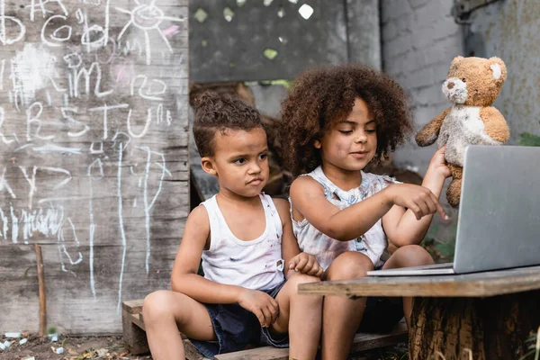 Selective focus of poor african american kid pointing with finger at laptop outside — Stock Photo