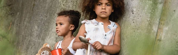 Panoramic orientation of african american kids begging alms near concrete wall in slum — Stock Photo