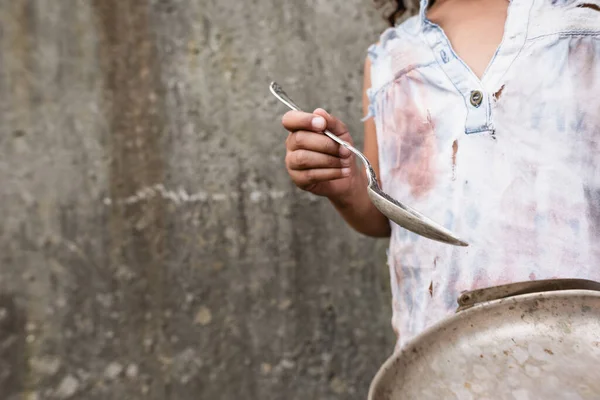 Vista recortada de niño afroamericano sosteniendo placa de metal y cuchara sucia en la calle urbana - foto de stock