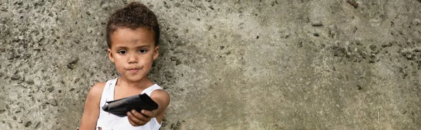 Plan panoramique d'un enfant afro-américain tenant un sac à main près d'un mur de béton dans une rue urbaine — Photo de stock