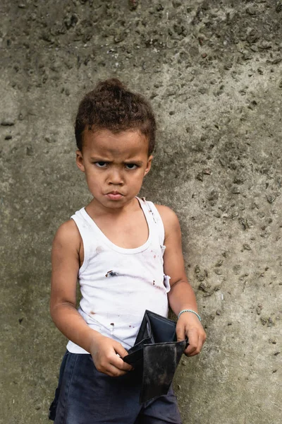 Angry african american child in messy clothes holding empty wallet on urban street — Stock Photo