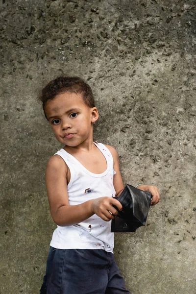 Mendigo afro-americano menino segurando carteira perto de parede de concreto na rua urbana — Fotografia de Stock