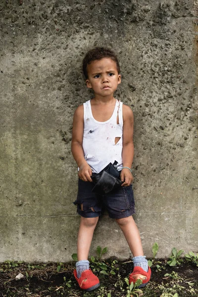 Inquiète garçon afro-américain en vêtements sales tenant portefeuille vide dans la rue urbaine — Photo de stock