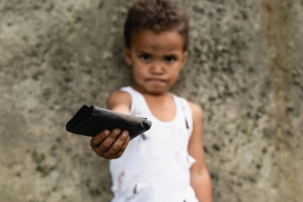 Concentration sélective d'un enfant afro-américain pauvre tenant un portefeuille dans une rue urbaine — Photo de stock