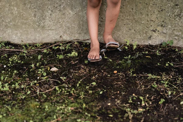 Обрізаний вид на ноги бідної афроамериканської дитини на землі біля бетонної стіни на відкритому повітрі — стокове фото