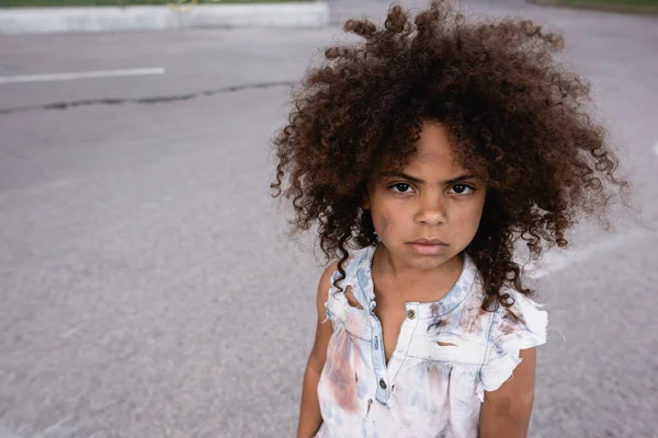 Pobre niño afroamericano con la cara desordenada mirando la cámara en la calle urbana - foto de stock