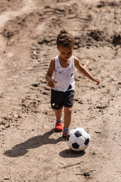 Armer afrikanischer amerikanischer Junge spielt Fußball auf schmutziger Straße in der Stadt — Stockfoto