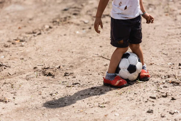 Ausgeschnittene Ansicht eines mittellosen afrikanisch-amerikanischen Kindes, das auf dem Boden einer städtischen Straße Fußball spielt — Stockfoto