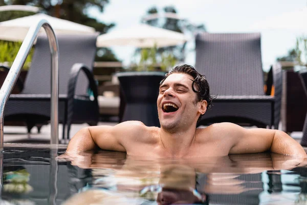 Selective focus of excited and wet man laughing in swimming pool — Stock Photo