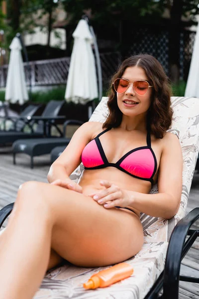 Fröhliches Mädchen mit Sonnenbrille trägt Sonnencreme am Bein auf — Stockfoto