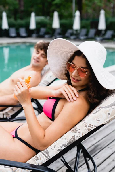 Selektiver Fokus attraktiver Mädchen mit Strohhut und Sonnenbrille, die Sonnencreme auftragen — Stockfoto