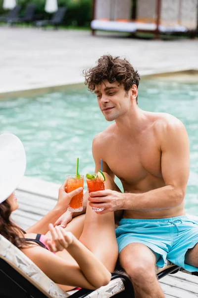 Мускулистый мужчина держит коктейль во время звона с девушкой в соломенной шляпе — стоковое фото