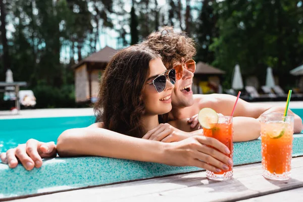 Glückliches Paar mit Sonnenbrille lächelt in der Nähe von Alkoholcocktails — Stockfoto