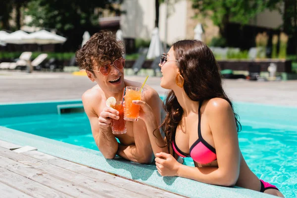 Allegro coppia clinking mentre tiene cocktail in piscina — Foto stock