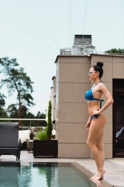 Barefoot woman in sunglasses standing near swimming pool — Stock Photo