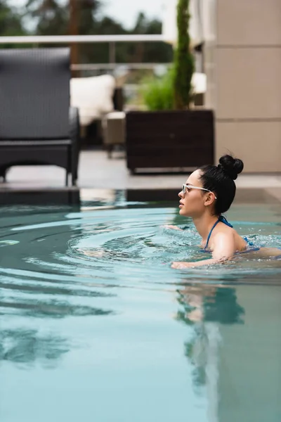 Vista lateral da menina atraente em óculos de sol nadando na piscina — Fotografia de Stock