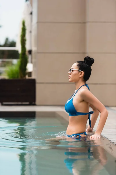Vista lateral de chica atractiva en gafas de sol nadando en piscina - foto de stock